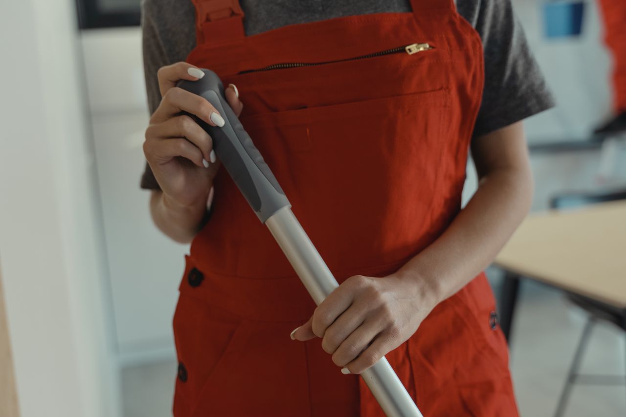A woman in a red apron holding a mop handle, performing cleaning indoors.
